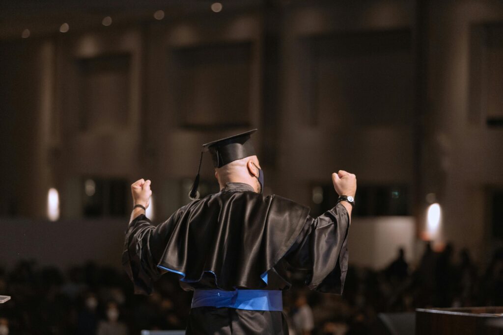 Graduate celebrating success at ceremony with arms raised in joy.