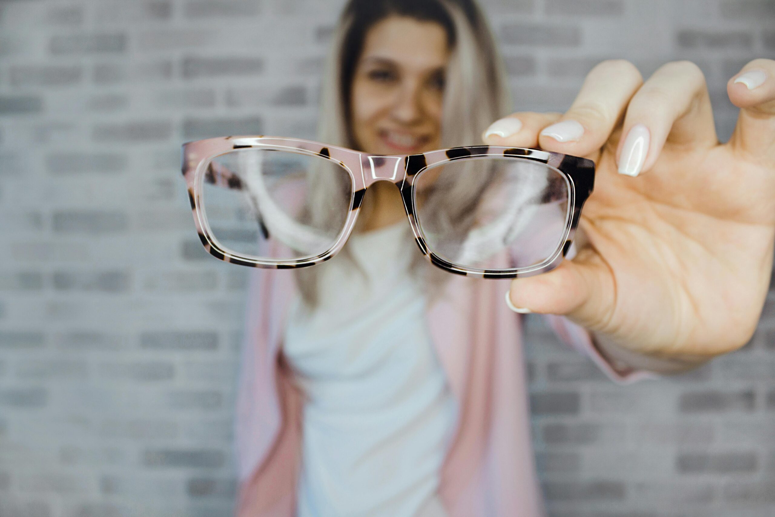 Young woman with blonde hair holding eyeglasses indoors, focusing on vision aid.