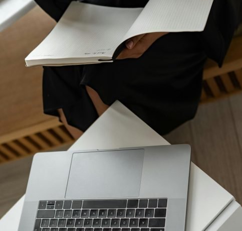 A woman multitasks with a laptop and notebook, symbolizing online education and productivity.